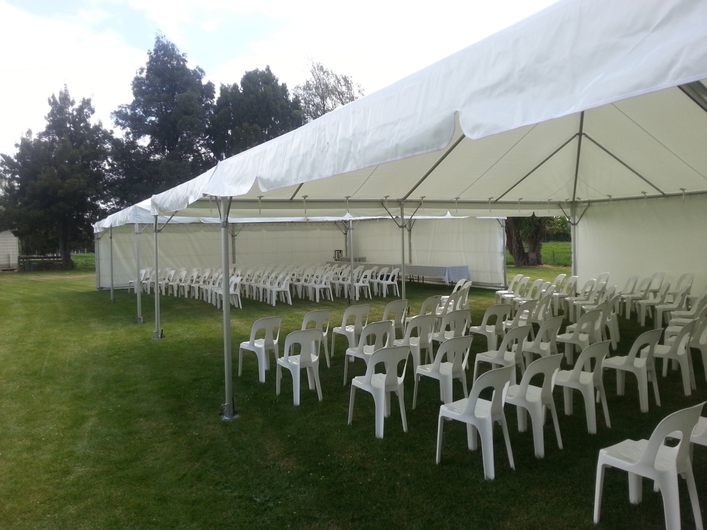 White ceremony chairs arranged beneath an open-sided marquee