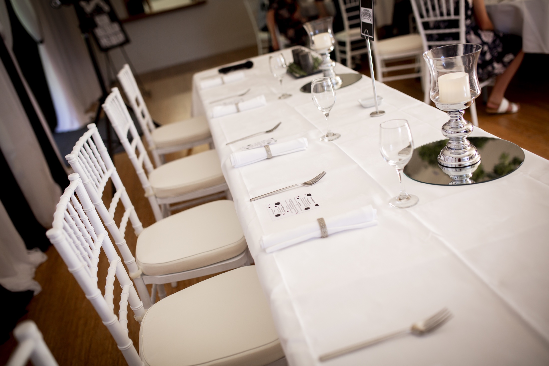 White wedding reception table with glassware and Chiavari chairs